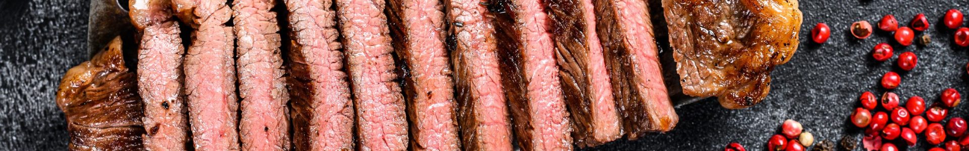 Grilled strip loin steak on a cleaver. The cooking medium. Black background. Top view.